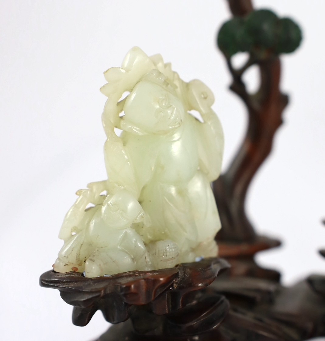 An assembled group of four Chinese pale celadon jade figures, 18th/19th century, displayed on two later wood 'rock-work' stands, total height approximately 19cm high